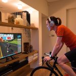Evde trainer üzerinde bisiklet süren sporcu, ekranda Zwift antrenmanını takip ediyor