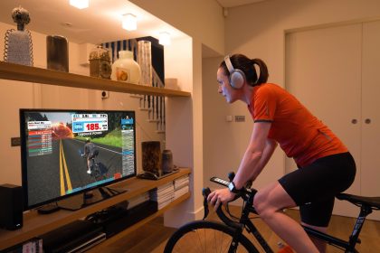 Evde trainer üzerinde bisiklet süren sporcu, ekranda Zwift antrenmanını takip ediyor