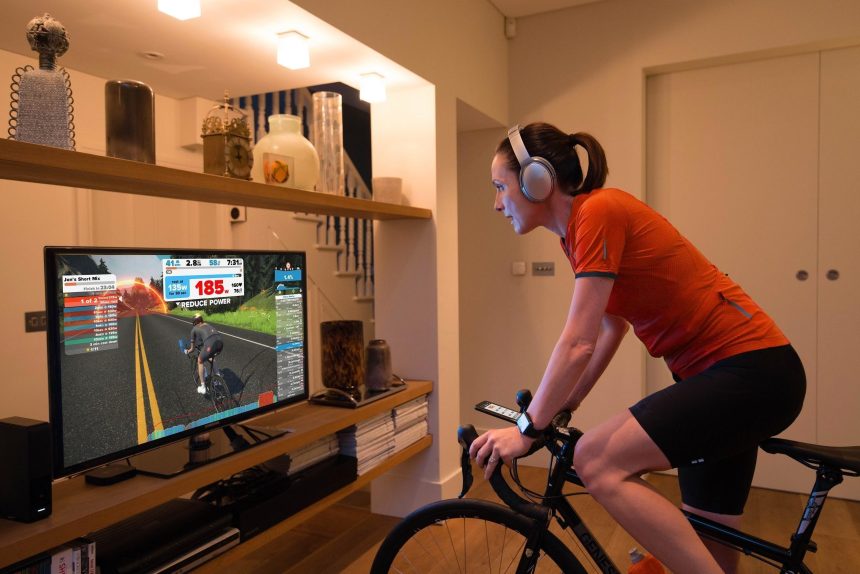 Evde trainer üzerinde bisiklet süren sporcu, ekranda Zwift antrenmanını takip ediyor